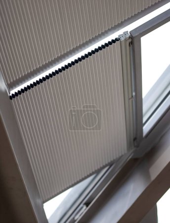 Motorized pleated blinds on the roof windows. Blinds for skylights, beige color. Honeycomb pleated blinds on glass roof.
