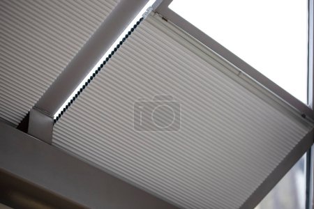 Téléchargez les photos : Motorized pleated blinds on the roof windows. Blinds for skylights, beige color. Honeycomb pleated blinds on glass roof. - en image libre de droit