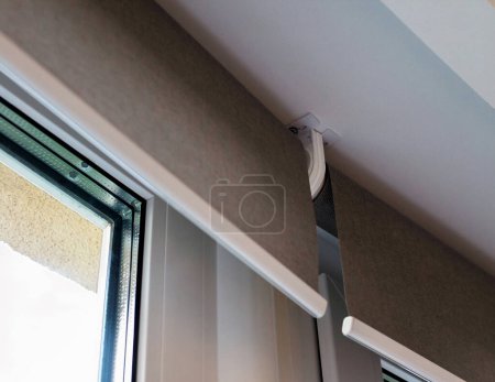 Photo for Roller blinds close up on the window. The distance between the fabrics when installing roller shades end-to-end. Intermediate bracket. Selective fokus. Motorized curtains. Beige color. - Royalty Free Image