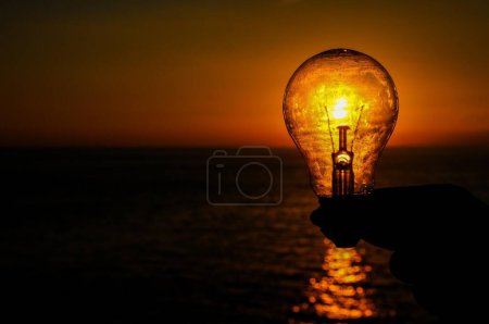 Energiekonzept Glühbirne und Sonnenuntergang am Atlantik