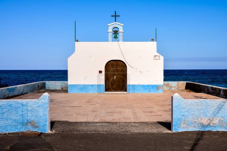 A small white church with a blue roof sits on a beach