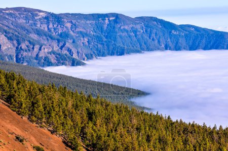 Ein Gebirge mit nebligem Himmel und einem Gewässer in der Ferne. Der Nebel ist dicht und die Berge sind von Bäumen bedeckt. Die Szene ist friedlich und heiter