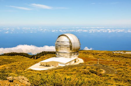 A large telescope is on a hill overlooking the ocean. The sky is clear and the sun is shining brightly