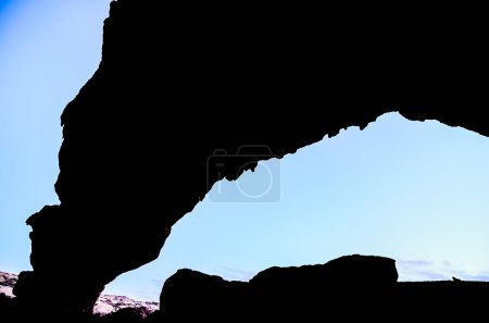 A dark cave with a view of the sky. The sky is blue and the sun is setting