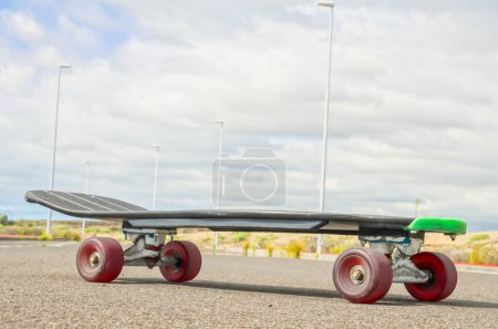 A skateboard is sitting on the ground with its wheels up. The sky is cloudy and the sun is not visible