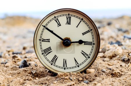 Die klassische analoge Uhr im Sand in der Felsenwüste