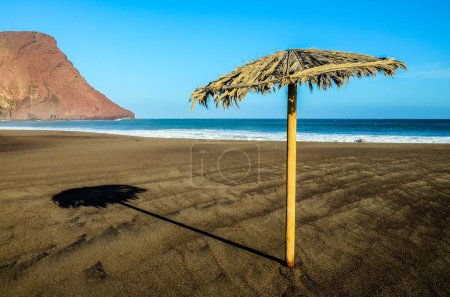 Un paraguas de playa está de pie en la arena en una playa. El paraguas es lo único visible en la imagen