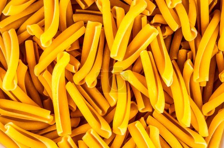 Eine Nahaufnahme von gelber Pasta. Die Nudeln sind lang und dünn und werden übereinander gestapelt. Das Bild hat ein warmes und einladendes Gefühl, als wäre es eine köstliche Mahlzeit, die darauf wartet, verzehrt zu werden