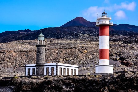 A lighthouse and a small building are on a rocky hillside. The lighthouse is red and white, and the building is white. The scene is peaceful and serene, with the lighthouse standing tall