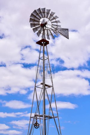 A windmill is tall and has a large, round top. The sky is blue and cloudy