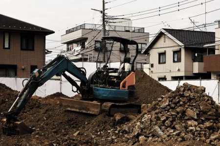 Téléchargez les photos : Un chantier de génie civil dans une zone résidentielle où une petite pelle est utilisée pour niveler le sol - en image libre de droit
