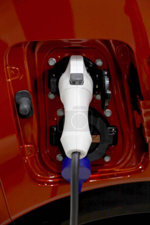 Foto de primer plano de un conector para cargar conectado a un coche eléctrico rojo