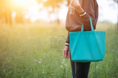 Photo for Young woman holding emerald green tote bag, no face, with sun shine, eco lifestyle concept - Royalty Free Image