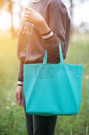 Foto de Mujer joven sosteniendo bolsa verde, sin rostro, con sol - Imagen libre de derechos