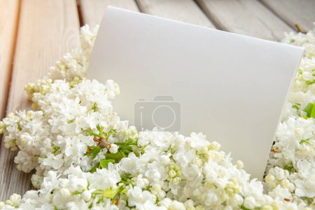 Téléchargez les photos : Carte blanche en papier vide avec fleurs lilas blanches et toile de fond en bois - en image libre de droit