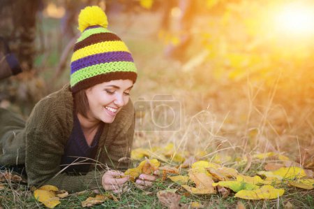 Foto de Retrato de mujer sonriente joven, descansando al aire libre en el parque, vestido con sombrero de punto con pompón - Imagen libre de derechos