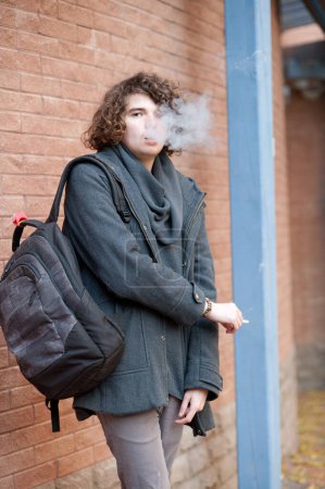 Photo for Portrait of a young handsome man, standing against brick wall and smoking a cigarette - Royalty Free Image