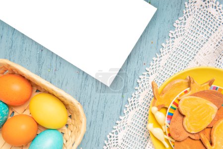 Téléchargez les photos : Liste blanche de papier vide avec des oeufs de couleur de Pâques et des biscuits maison de vacances sur une assiette - en image libre de droit