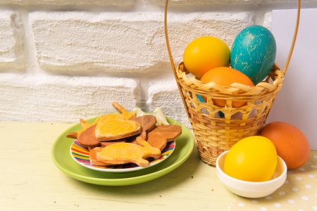 Téléchargez les photos : Carte de Pâques avec panier avec oeufs de couleur Pâques et assiette avec biscuits de vacances sur une table de cuisine - en image libre de droit