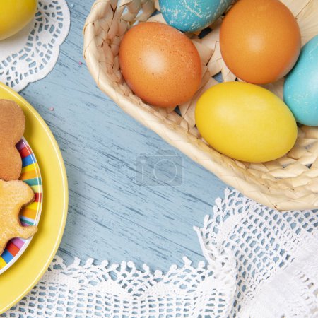 Foto de Easter table template with colored eggs and holiday cookies on a blue backdrop, top view - Imagen libre de derechos