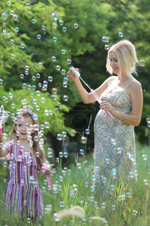 Foto de Niña con su mamá embarazada divertirse soplando burbujas en el parque - Imagen libre de derechos