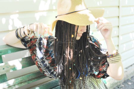 Téléchargez les photos : Joyeuse jeune femme portrait avec dreadlocks habillé dans la robe de style boho et chapeau, extérieur ensoleillé, couleurs vintage - en image libre de droit