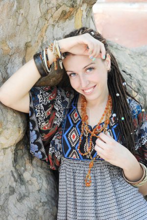 Téléchargez les photos : Joyeuse jeune femme portrait avec dreadlocks coiffure posant dans un parc extérieur ensoleillé, regardant la caméra - en image libre de droit