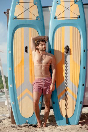 Téléchargez les photos : Jeune surfeur homme portrait extérieur posant près d'une planche de surf - en image libre de droit