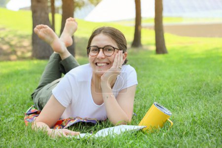 Foto de Mujer estudiante feliz tomar un descanso en un parque en una hierba, sonriendo y mirando a la cámara - Imagen libre de derechos