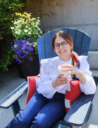 Téléchargez les photos : Jolie jeune femme se reposer dans un café en plein air avec une tasse de café, des fleurs sur fond - en image libre de droit