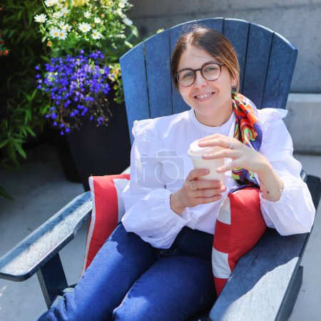 Téléchargez les photos : Jolie jeune femme se reposer dans un café en plein air avec une tasse de café, des fleurs sur fond - en image libre de droit