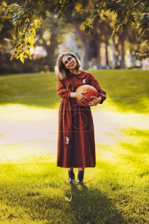 Téléchargez les photos : Belle jeune femme ont un loisir debout avec citrouille dans les mains dans le parc d'automne - en image libre de droit