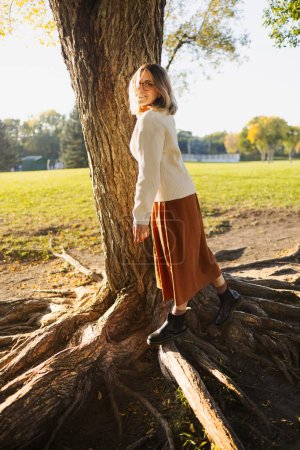 Photo for Beautiful young woman have a leisure posing in autumn park dressed in long brown skirt and white sweater - Royalty Free Image