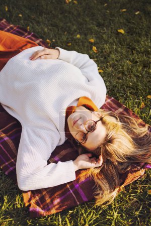 Foto de Hermosa mujer joven tienen un ocio posando en el parque de otoño vestido con falda larga marrón y suéter blanco - Imagen libre de derechos