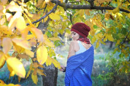 Téléchargez les photos : Happy souriant portrait de femme en plein air dans le parc, vêtu d'un chapeau rouge tricoté et d'un pull bleu - en image libre de droit