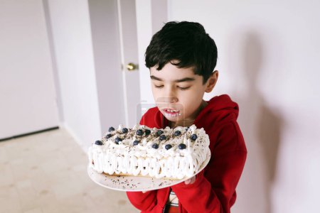 Téléchargez les photos : Mignon garçon tenant maison tarte aux myrtilles avec crème blanche et regarder sur elle - en image libre de droit