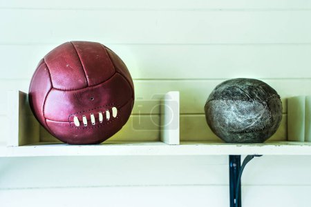 Foto de Bola de fútbol de cuero rojo oscuro y jugar pelota en estilo retro que se encuentra en un estante - Imagen libre de derechos
