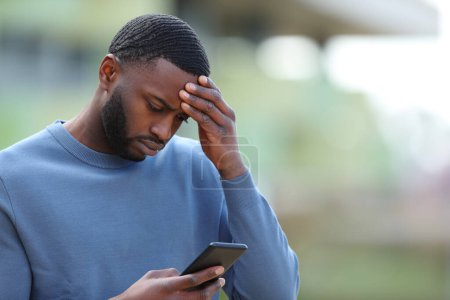Photo for Concerned black man reading bad news on smart phone in the street - Royalty Free Image