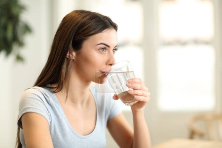 Frau trinkt zu Hause Wasser aus Glas