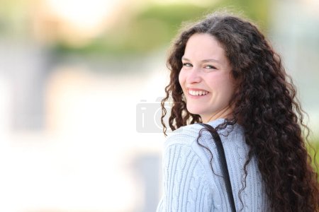 Foto de Happy woman posing and smiling in the street twirling to look at camera - Imagen libre de derechos