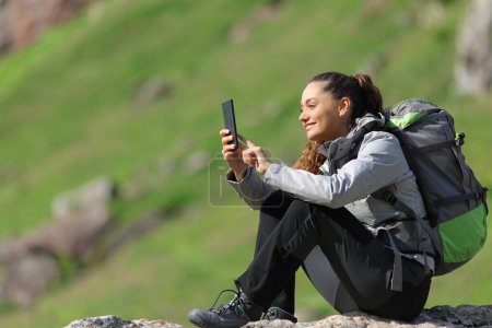 Foto de Caminante feliz usando el teléfono inteligente sentado en la naturaleza - Imagen libre de derechos