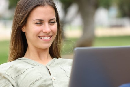 Teen laughing checking laptop sitting in a park Poster 648035386