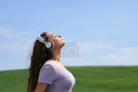 Side view portrait of a woman meditating in a field listening audio guide with headphone
