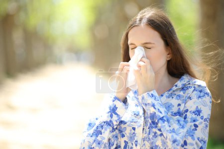 Femme allergique soufflant sur les tissus marchant en été dans un parc