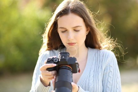 Téléchargez les photos : Un photographe sérieux vérifie un écran de caméra sans miroir dans un parc - en image libre de droit