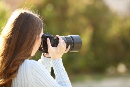 Rückseite Porträt eines Fotografen, der mit spiegelloser Kamera in einem Park fotografiert