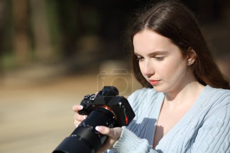 Serious photographer checking pictures on mirrorless camera outdoors