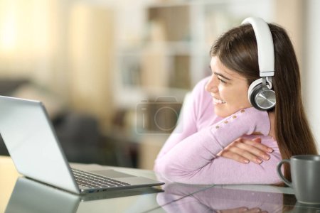 Foto de Feliz adolescente viendo videos en el portátil y auriculares sentados en casa - Imagen libre de derechos
