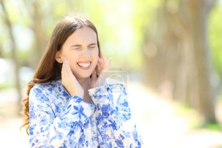 Photo for Woman suffering mandibular ache standing in a park - Royalty Free Image