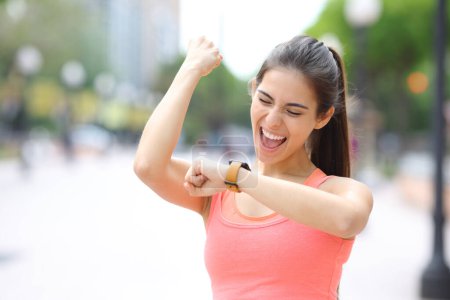 Photo for Excited runner celebrating good time checking smartwatch in the street - Royalty Free Image
